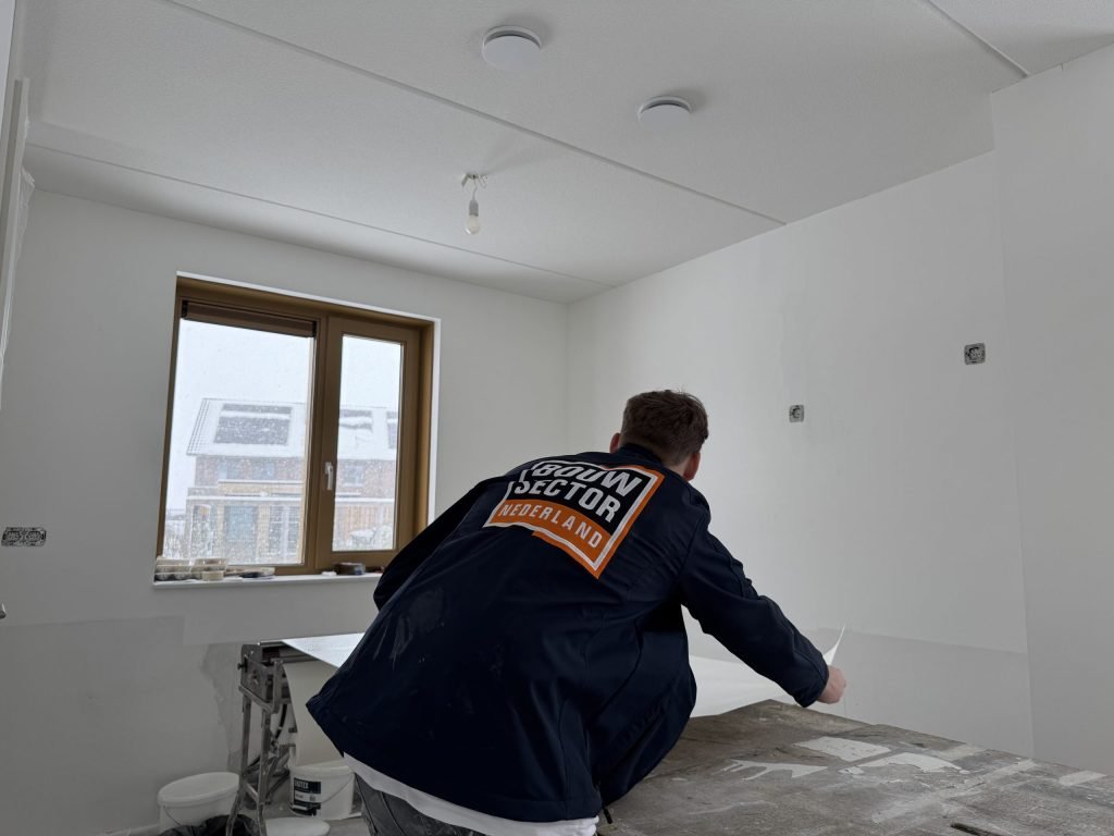 Vakman van Bouwsector Nederland legt een baan vlies op de plaktafel in een kamer met kale wanden