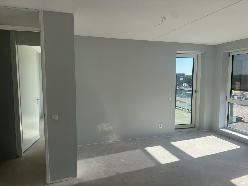 Kamer met lichtgrijs gesausde wanden, een balkondeur en een betonvloer