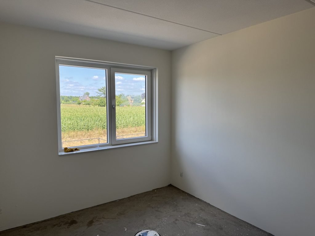 Lege nieuwbouwslaapkamer met strak gesausde wanden en uitzicht over een maisveld