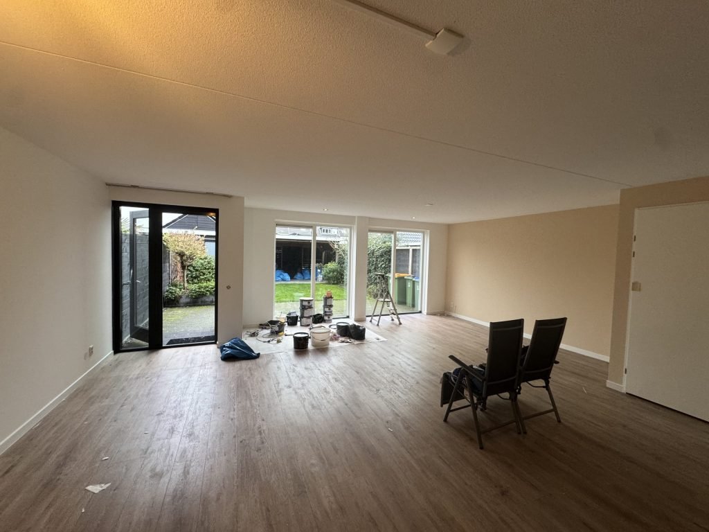 Woonkamer van een bestaande woning tijdens de afwerking, met verfemmers bij de tuindeuren en twee stoelen