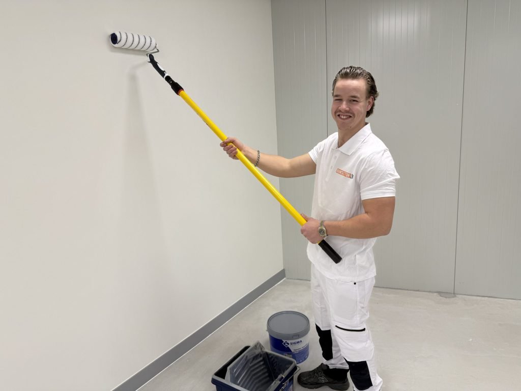 Schilder van Bouwsector Nederland saust een witte wand met een roller aan een steel, met een emmer Sigma-verf