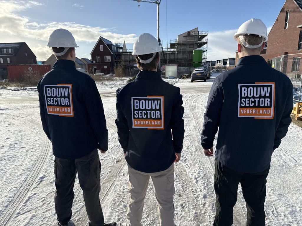 Drie vakmensen van Bouwsector Nederland met witte helm en bedrijfsjas bij een bouwplaats in de sneeuw